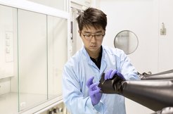 A scientist in a white lab coat and purple gloves examines the pushed out gloves of a glove box.