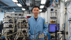 Blue lab coat-clad individual stands amidst complex electronic apparatus and monitoring devices in a lab.