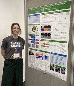 Person next to a poster presenting research on frequency multiplication in ferromagnetic microstructures.